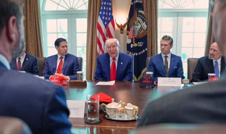 Donald Trump meets with advisors at a conference table, discussing national security amid the escalating Israel-Iran conflict, with American flags and presidential seal in the background.