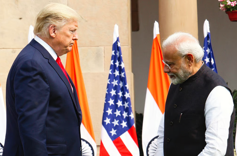 Prime Minister Narendra Modi shaking hands with former US President Donald Trump during a joint event, with Indian and American flags in the background.
